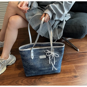 Detail of blue denim tote bag with silver glitter finish and white pearl lace bow charm