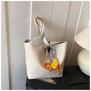 Detailed macro view of the cream tote bag showing pebbled leather texture and elephant charm