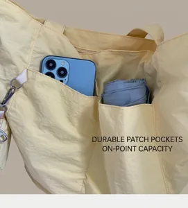 Pale yellow waterproof nylon tote bag detail showing large pockets holding phone and umbrella