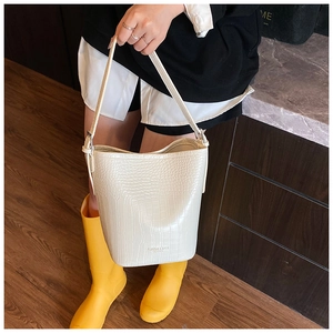 Close-up of beige crocodile embossed bucket bag with long shoulder strap detail