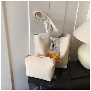 Detail view of cream tote bag with matching zipper pouch and elephant charm on textured leather