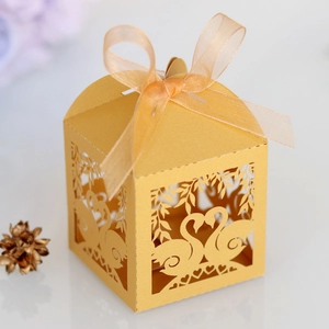 Close-up of laser-cut wedding favor box with swan pattern and elegant gold ribbon