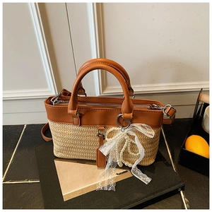 Detail of straw woven tote bag featuring brown leather trim and lace bow decoration