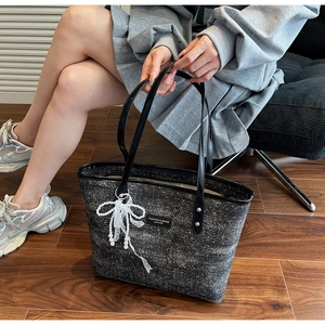 Detail of a black textured tote bag featuring a pearl lace bow and leather handles
