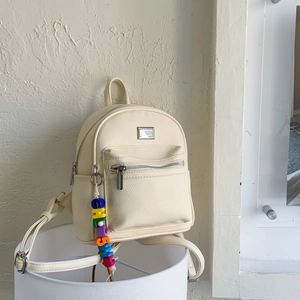 Détail du mini sac à dos crème avec cuir litchi et un pendentif lettres colorées