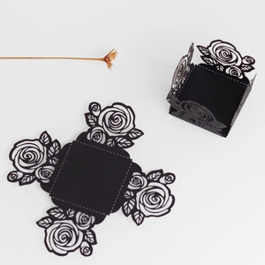 Détails de roses découpées au laser sur des boîtes cadeaux noires plates et pliées
