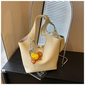 Detail of cream leather tote bag featuring a colorful elephant charm and lychee texture