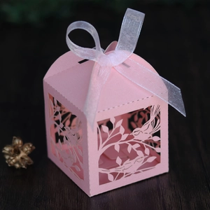 Detail of laser-cut love bird patterns on a pink wedding favor box with a white ribbon