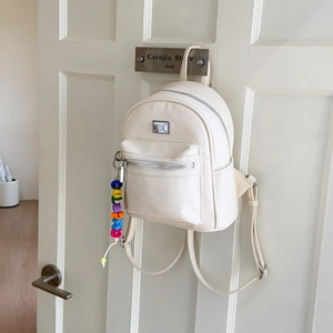 Gros plan du mini sac à dos crème en cuir texturé avec un pendentif de lettres colorées