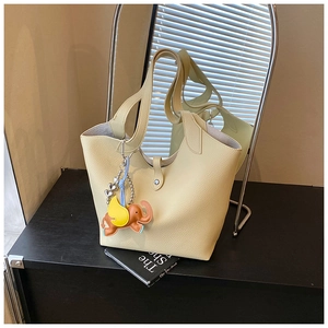 Detail of beige lychee leather tote bag with a cute orange elephant charm accessory