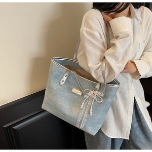 Detail of light blue tote bag with pearl tassel and lace bow detail on a shoulder strap