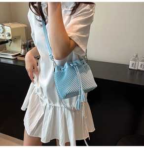 Detail of light blue woven bucket bag with tassel drawstring and silver chain strap
