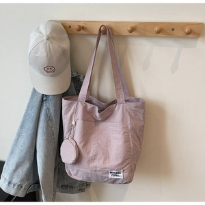 Pink canvas tote bag hanging on wooden rack with round coin purse and small woven label