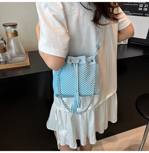 Detail of light blue woven bucket bag featuring drawstring closure and tassel decoration