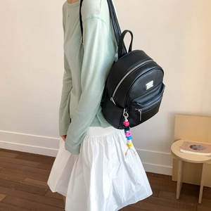 Gros plan du mini sac à dos en cuir noir grainé avec zip argenté et breloque perlée colorée