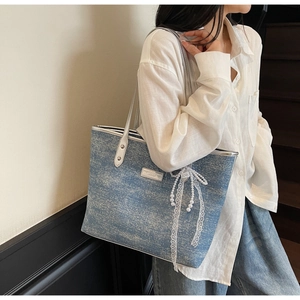 Detail of light blue denim tote bag with shiny texture and lace pearl bow charm
