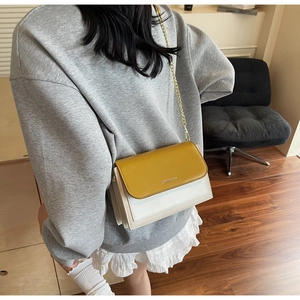 Detail of trendy color-block crossbody bag featuring yellow flap and gold chain strap