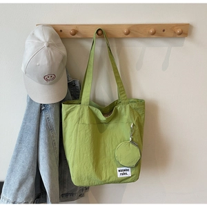 Close-up of a pea green canvas tote bag with round coin purse on a wooden wall hook