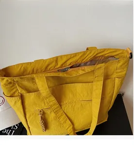 Detailed view of the yellow nylon tote bag featuring a smooth zipper and woven puller