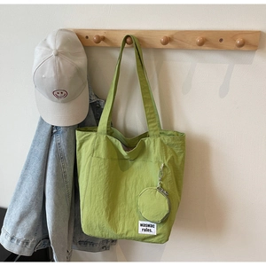 Close-up of grass green nylon tote bag with logo tag and a small matching round pouch