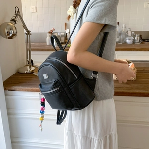 Détail d'un sac à dos en cuir noir avec un charm en perles colorées sur le zip