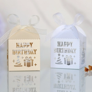 Detail of laser-cut Happy Birthday candy boxes in champagne and white with silk ribbons
