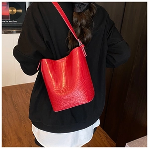 Detail of red crocodile pattern leather bucket bag worn by model on shoulder