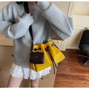 Detail of yellow leather bucket bag with brown strap and mini pouch on female model