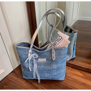 Detail of blue denim tote bag with silver handles, lace bow, and pearl charm accents