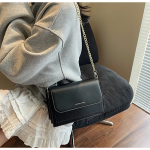 Close-up of black leather crossbody bag with gold chain strap and fashion lettering