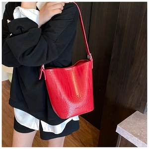 Detail of red crocodile texture bucket bag with adjustable strap on black outfit
