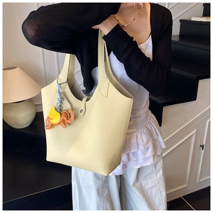 Detail view of cream tote bag with orange elephant charm shown on model in modern interior