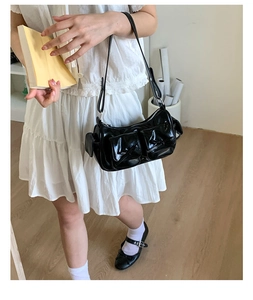 Détail d'un sac à bandoulière noir brillant avec poches ornées de nœuds décoratifs