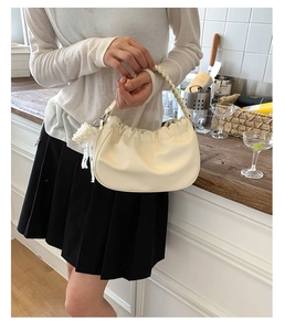 Detail of cream pleated cloud bag with pearl heart charm and woven handle detail