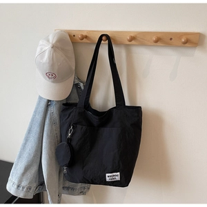 Detail of black canvas tote bag with logo tag and a white smiley face baseball cap
