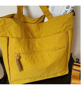 Close-up of a yellow tote bag featuring fabric texture and hand-woven zipper pullers