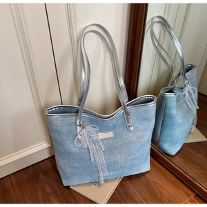 Detail of light blue denim tote bag with silver handles and white lace bow pendant