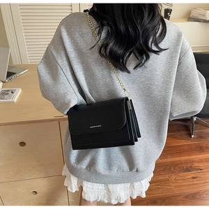 Detail of a black leather shoulder bag with gold chain strap worn in a modern office setting