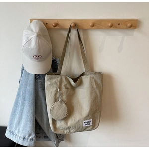 Detail of canvas tote bag with side pocket, hanging round coin purse and logo tag