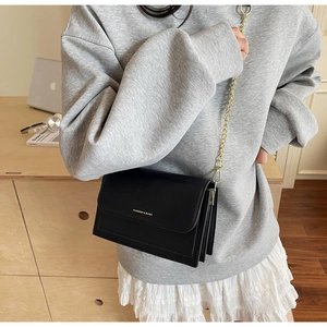 Detail of a black leather crossbody bag with gold chain strap on a casual outfit