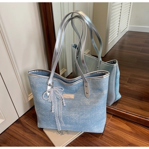 Macro detail of a light blue textured tote bag with a pearl lace bow and silver handle