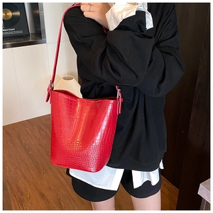 Detail of red crocodile pattern bucket bag with strap worn on a casual outfit