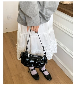 Détail du sac sous l'aisselle en cuir verni noir avec nœuds et poches frontales