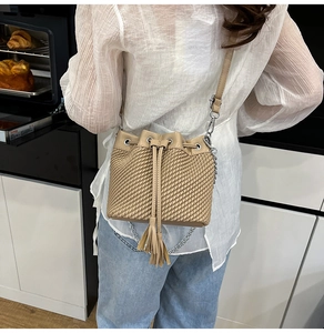 Lifestyle shot of women's beige woven bucket bag with tassel drawstring and chain strap