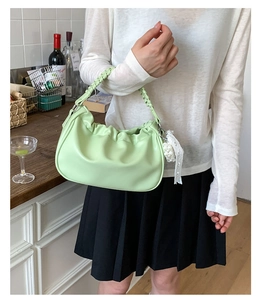 Close-up of pleated mint green shoulder bag with woven handle and pearl lace pendant