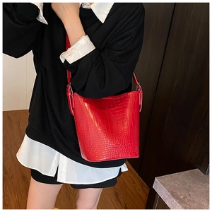 Detail of red crocodile pattern bucket bag with adjustable strap worn on the shoulder
