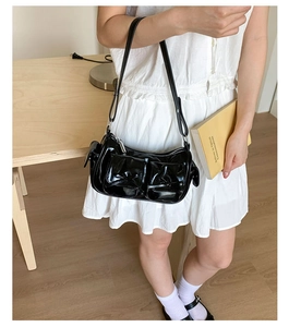 Détail du sac à bandoulière en cuir noir brillant avec poches et fermetures éclair argent