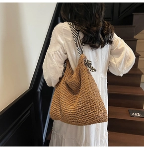 Detail of hand-woven straw tote bag with black and white striped shoulder strap
