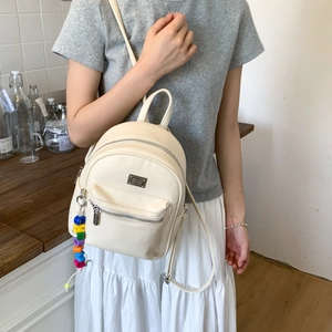 Détail du mini sac à dos crème avec texture cuir litchi et pendentif lettre coloré