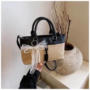 Close-up of straw woven tote bag with black leather accents and a lace bow with pearls